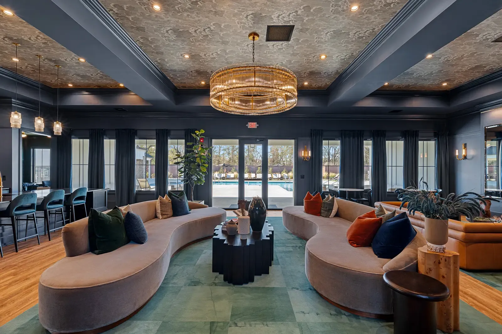 Stylish hotel lobby with curved sofas, colorful cushions, a central chandelier, elegant decor, and large windows overlooking a pool. Calm and inviting ambiance.